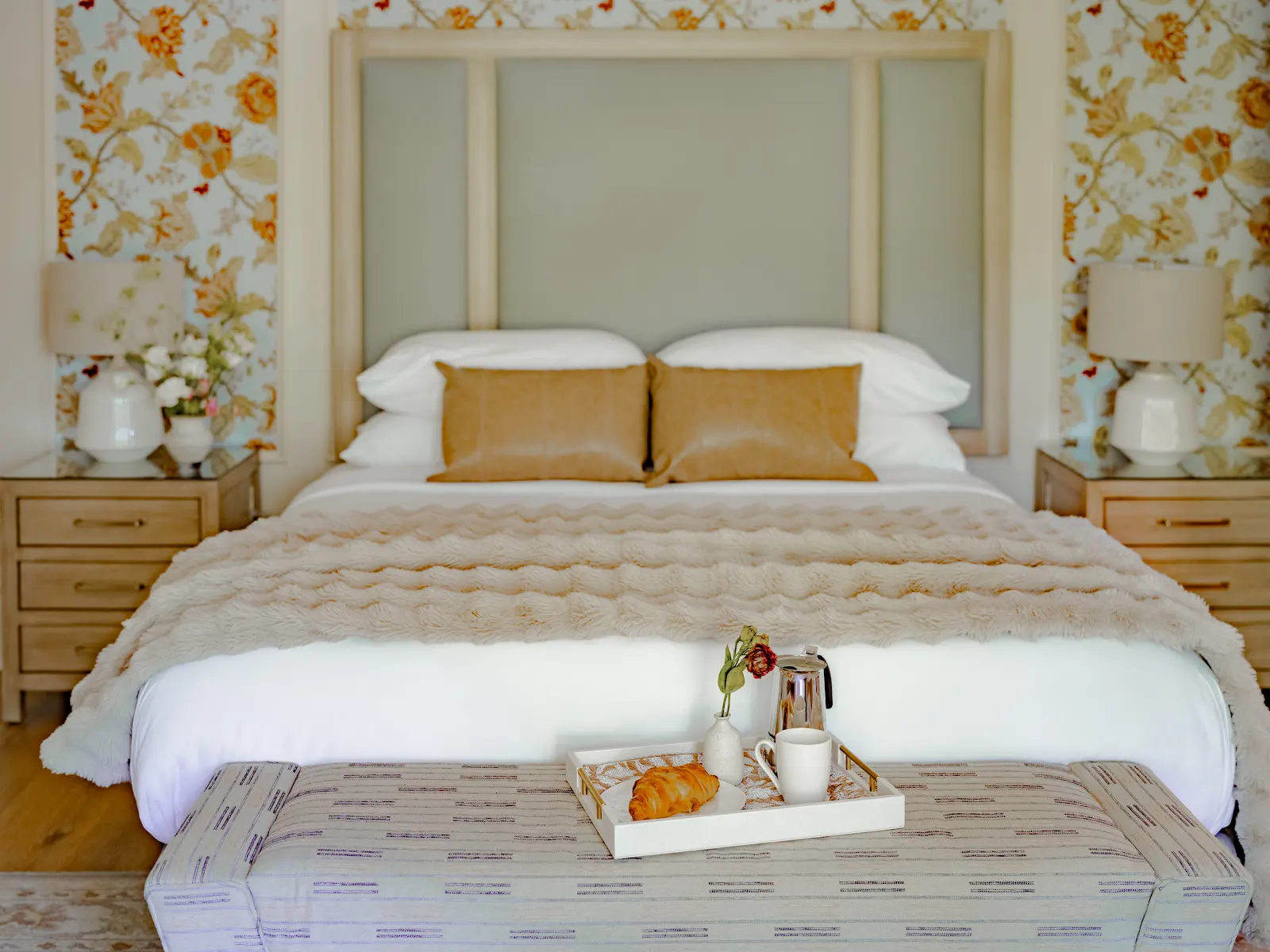 Breakfast with croissants and coffee on the bench at the foot of a bed in a floral-wallpapered Hennessey Estate room